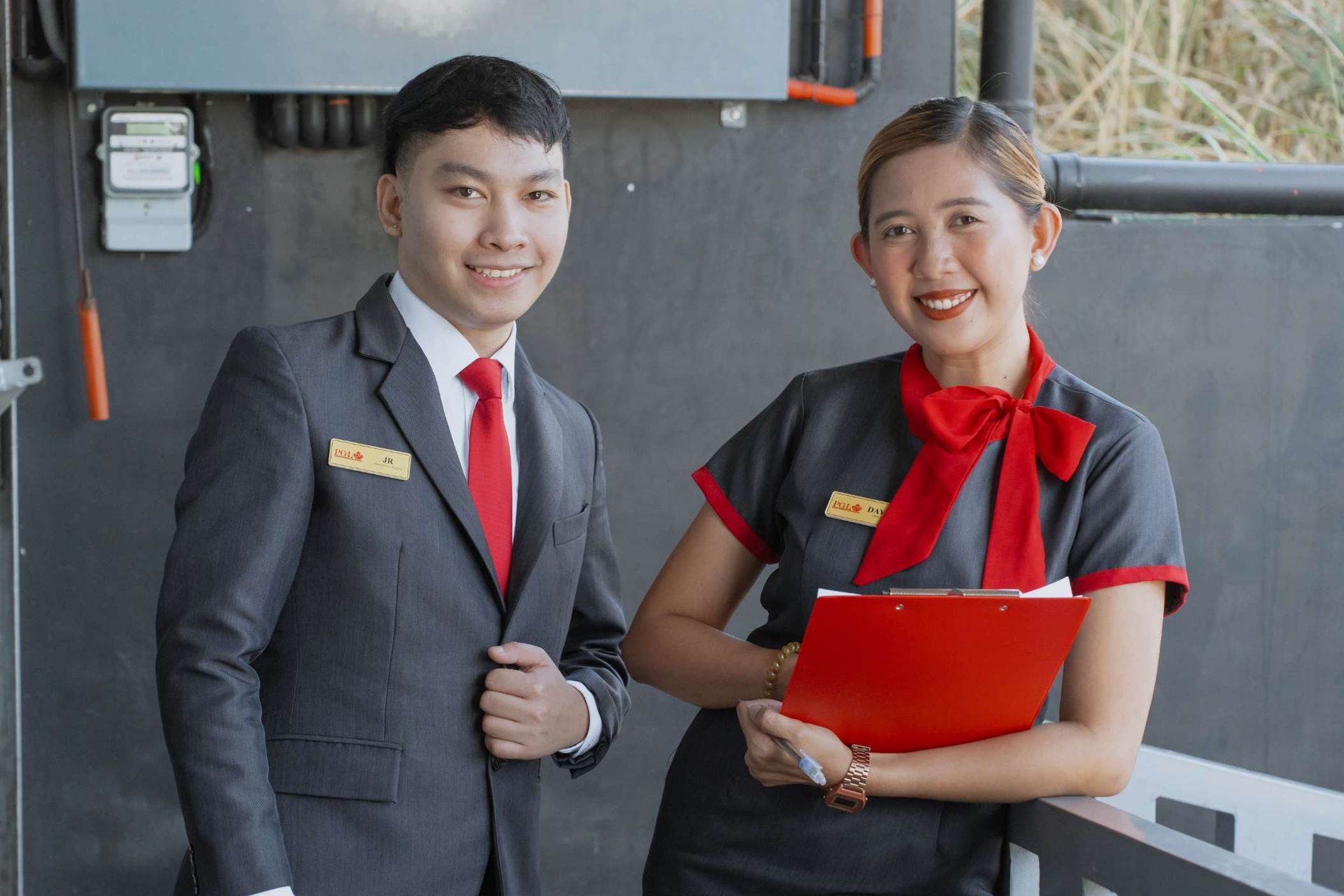A man in a suit and tie is standing next to a woman holding a clipboard.