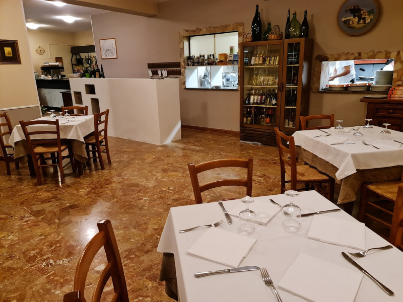 Interno di un ristorante con sedie in legno, tavoli apparecchiati con tovaglie bianche e una cantinetta per i vini con ante in vetro.