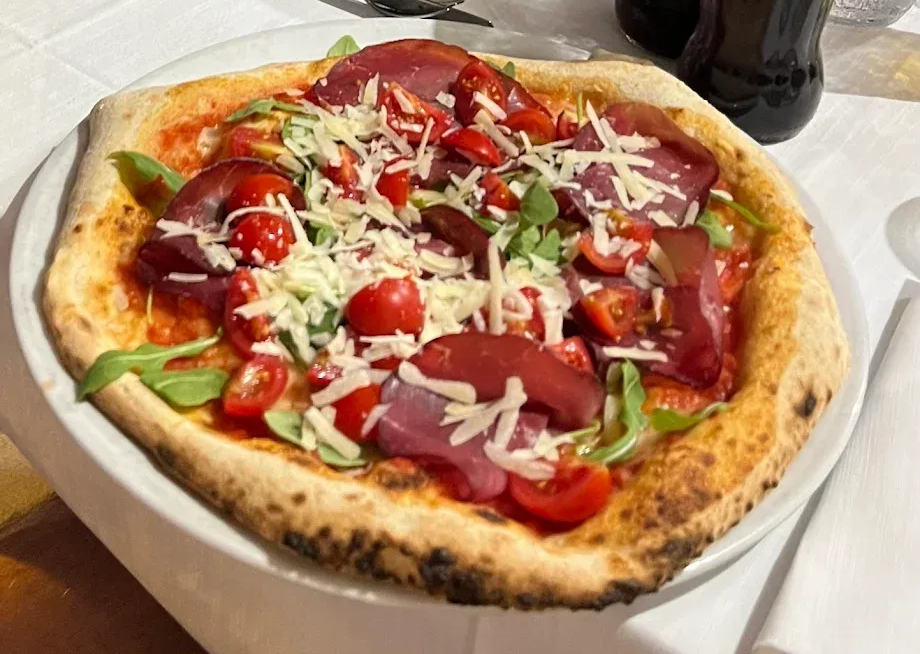 Una pizza condita con pomodorini, sottili fette di bresaola, rucola e formaggio grattugiato su un piatto bianco.