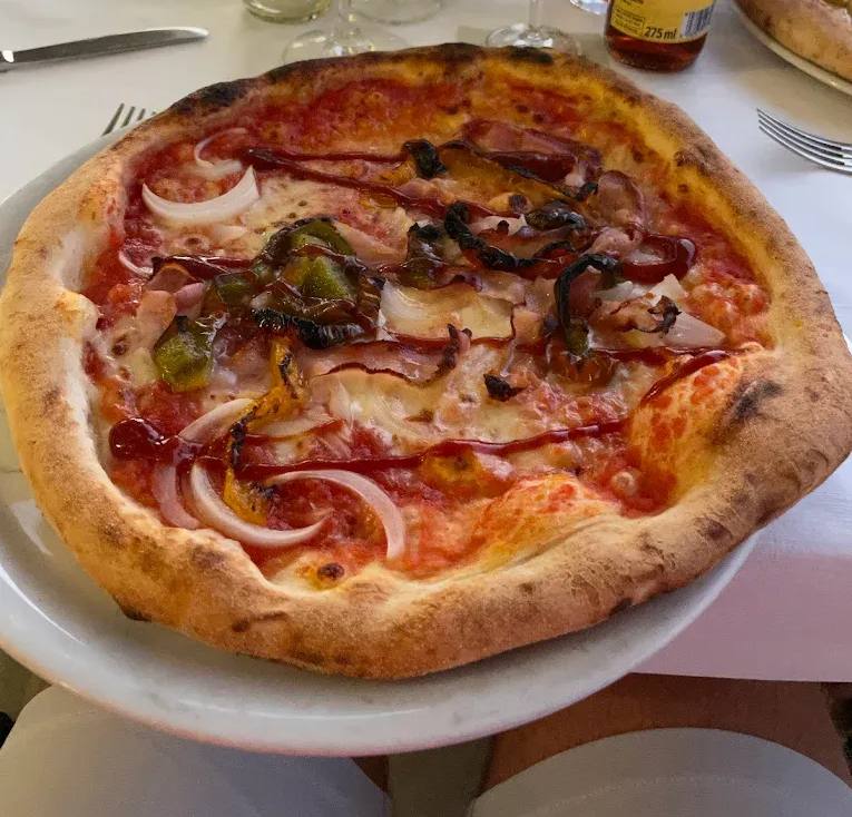 Una pizza cotta su un piatto, condita con salsa di pomodoro, cipolle, peperoni saltati e fili di glassa di aceto balsamico scuro.
