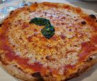 Una pizza a crosta sottile condita con formaggio fuso, salsa di pomodoro e una singola foglia di basilico al centro.