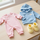 Ropa de bebé extendida sobre una mesa: un body rosa, una sudadera azul con capucha y unos patucos amarillos.