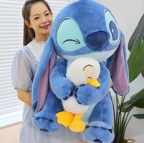 Un peluche azul de Stitch abraza a un peluche más pequeño de color blanco y amarillo en una habitación infantil soleada.