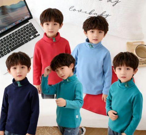 Cinco niños con coloridos cuellos de tortuga posando en el interior junto a una computadora portátil en una cama.