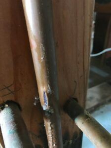 Leaking copper pipe with a blue patch against a wooden post.