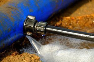 Leaking blue pipe with black coupling, water spraying out.