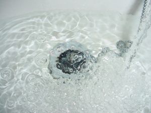 Water flowing into a sink, creating bubbles around the drain.