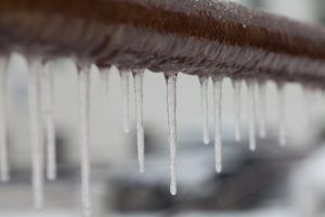 Icicles hanging from a brown pipe outdoors, blurred white background.