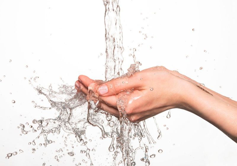 Hand cupped under running water, water splashing outward, white background.