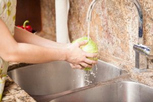 Person washing a cabbage under running water in a kitchen sink.