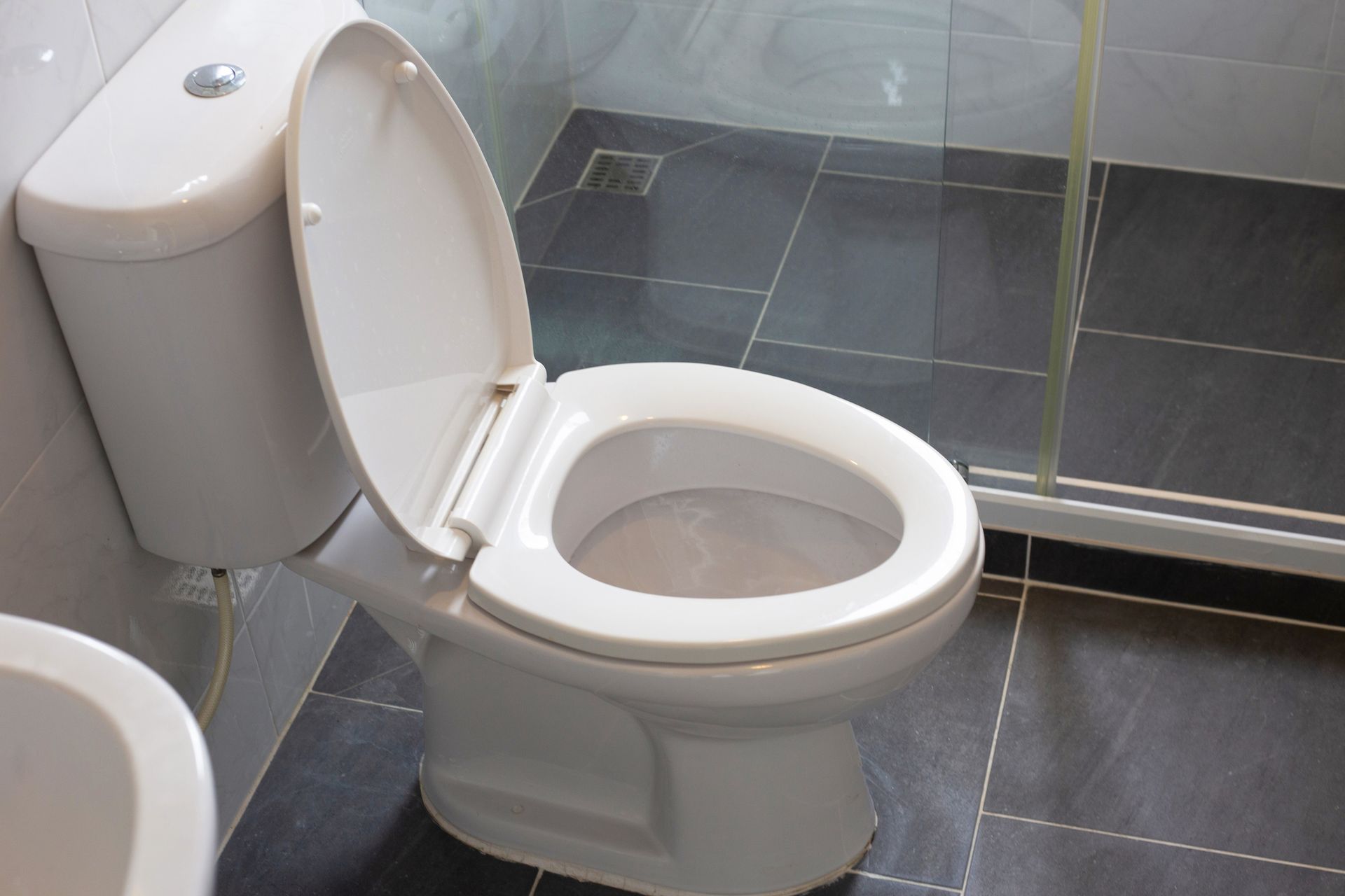 White toilet with open lid on a dark tiled floor in a bathroom.