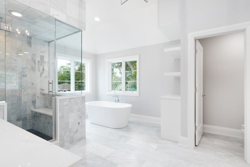 Bright white bathroom with glass shower, soaking tub, and window.