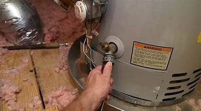 Hand reaching for a water heater drain valve. The heater is in an unfinished attic.