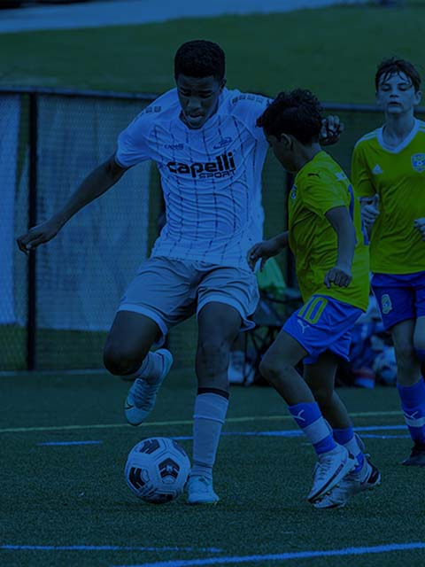 Soccer player in white dribbles past defenders in yellow on a field, ball at his feet