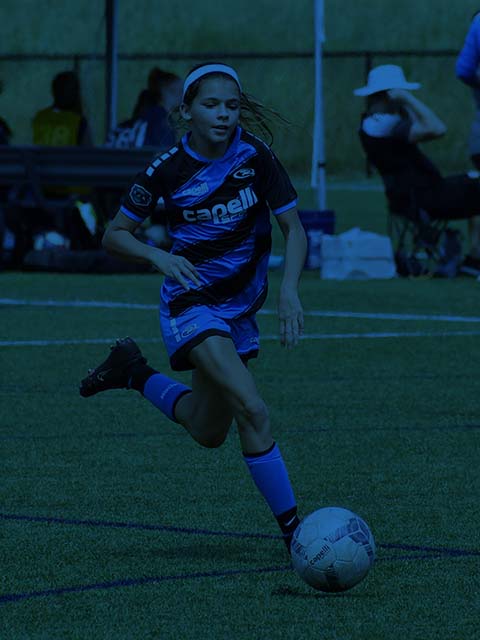 Soccer player in blue dribbles a ball on a field at night