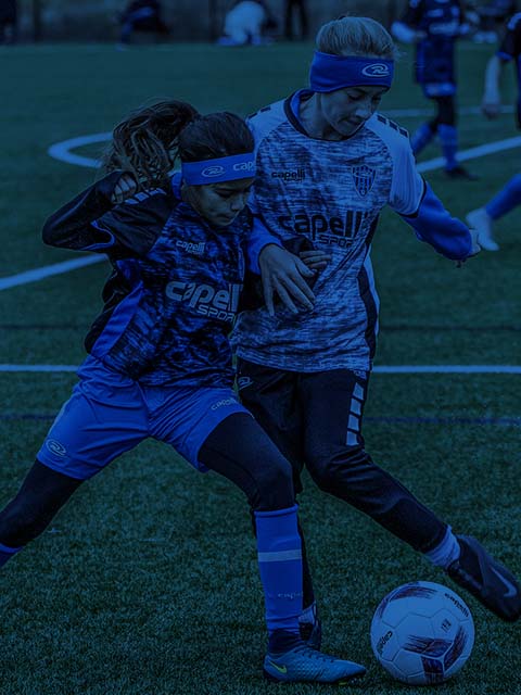 Two youth soccer players in blue uniforms vying for the ball on a field