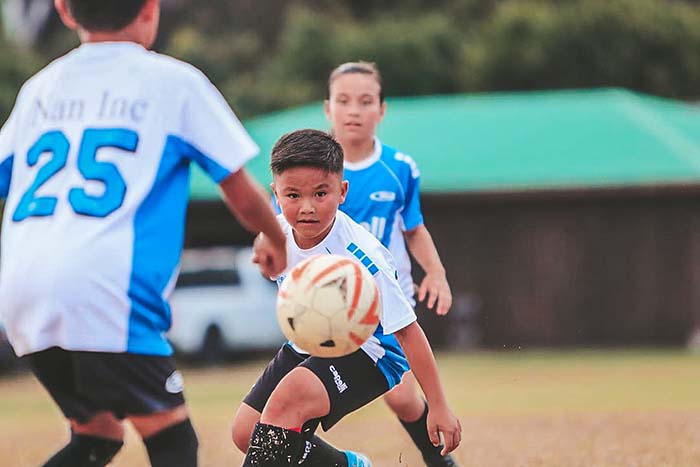 Youth soccer players in blue jerseys battling for the ball on a grassy field