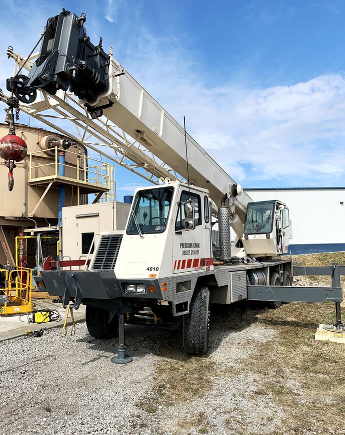 A truck with a crane attached to it is parked in a gravel lot.