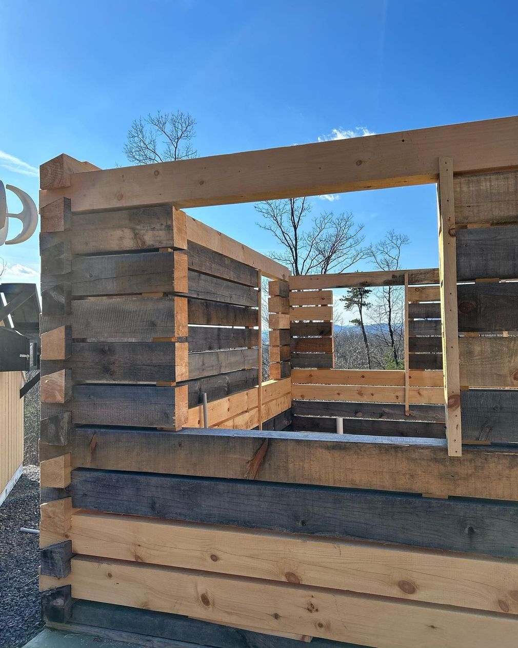 Wooden crate-like structure made of stacked lumber outdoors under a clear blue sky