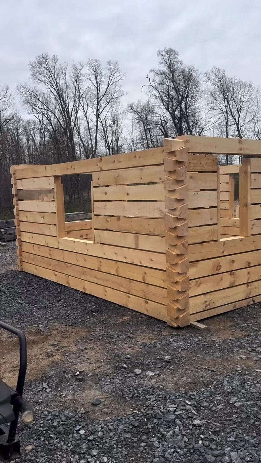 Partially built wooden cabin with window openings on a gravel lot under a cloudy sky