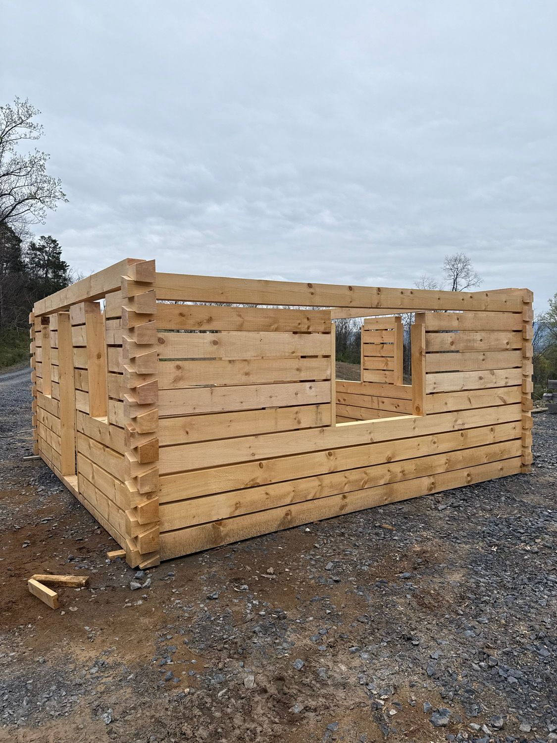 Partially built wooden cabin on a gravel lot under a cloudy sky