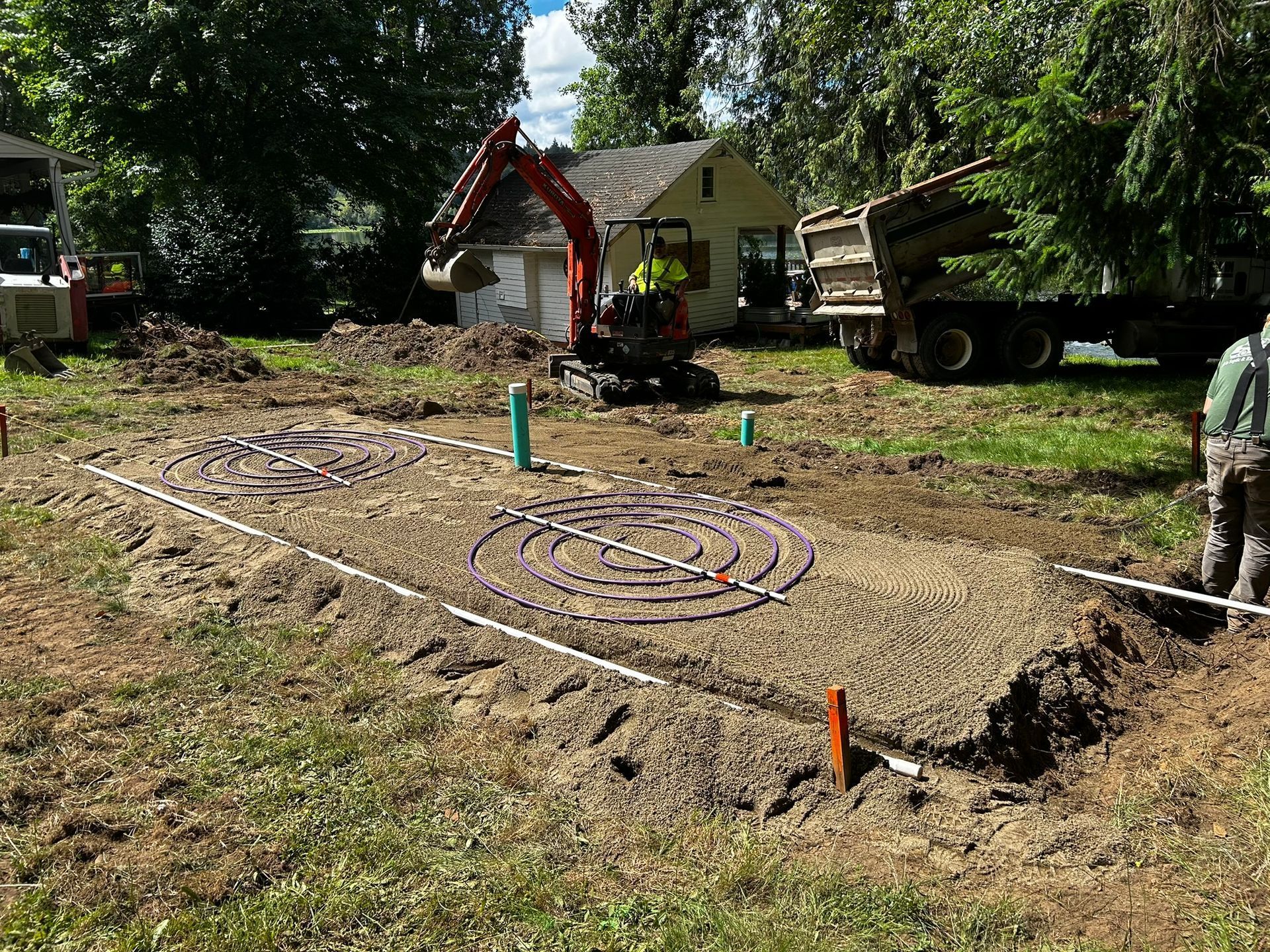 Construction site with excavator and dump truck; buried pipes and gravel beds.