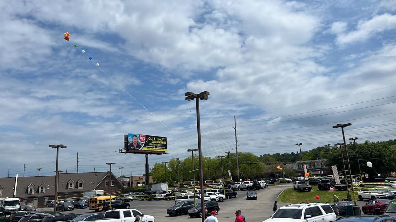 Busy parking lot with cars, a colorful billboard, and cloudy blue sky over low buildings