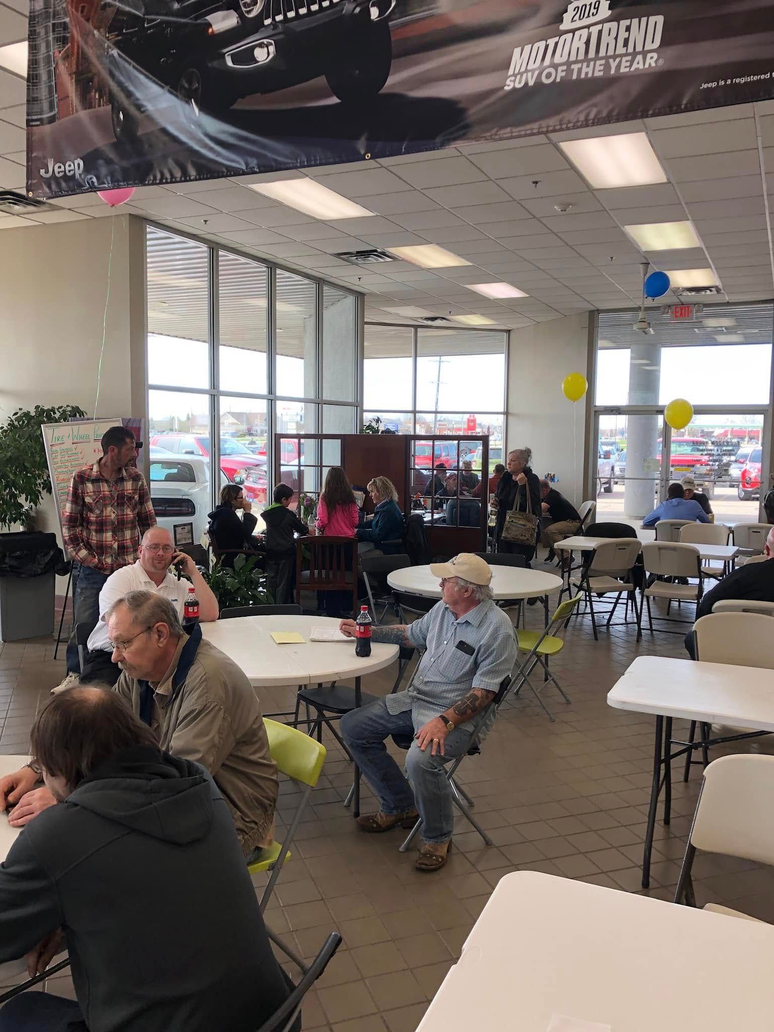 People seated at tables in a bright cafeteria with large windows and a glass entrance.