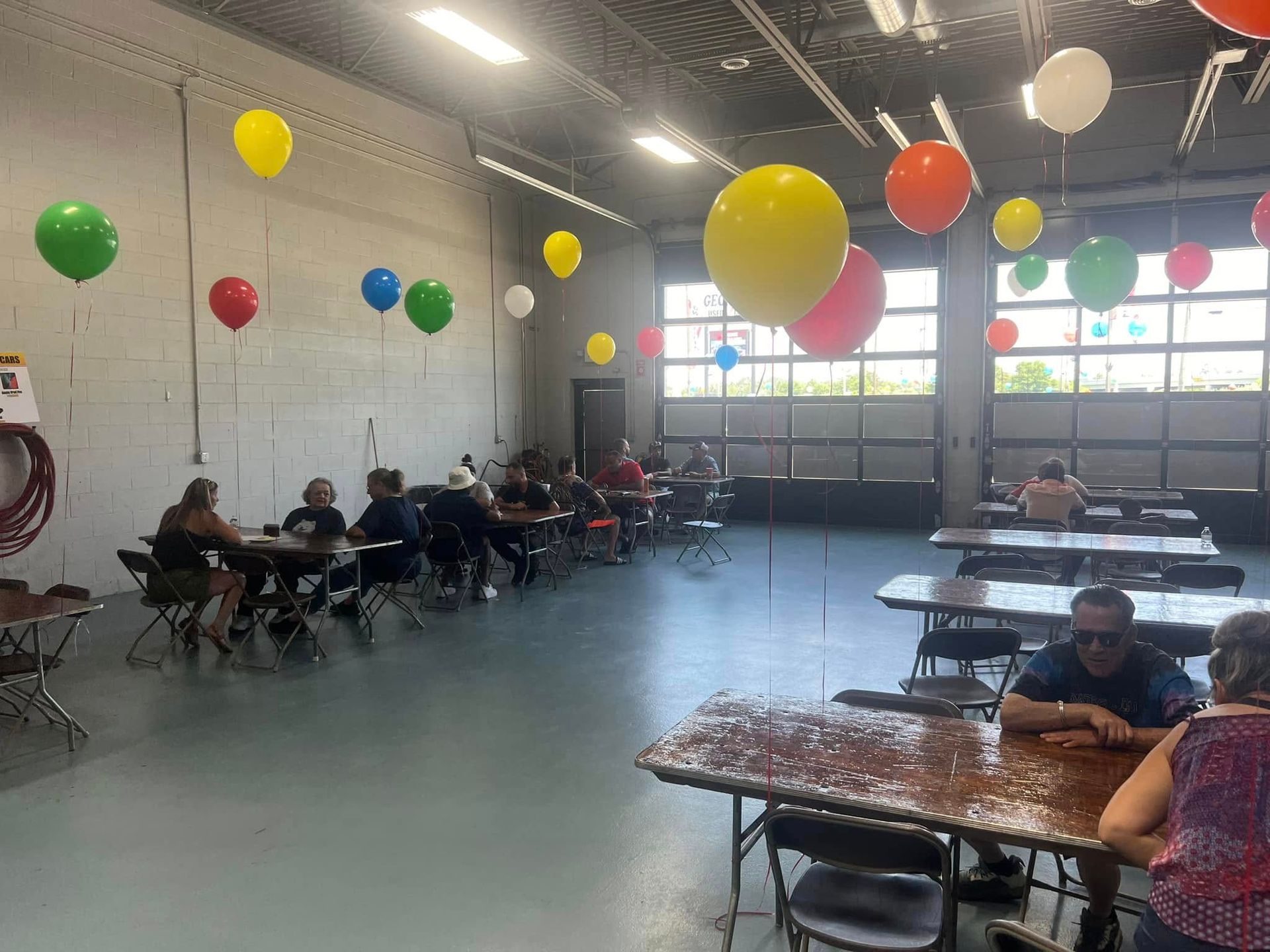 Large indoor hall with tables, seated people, and colorful hanging balloons