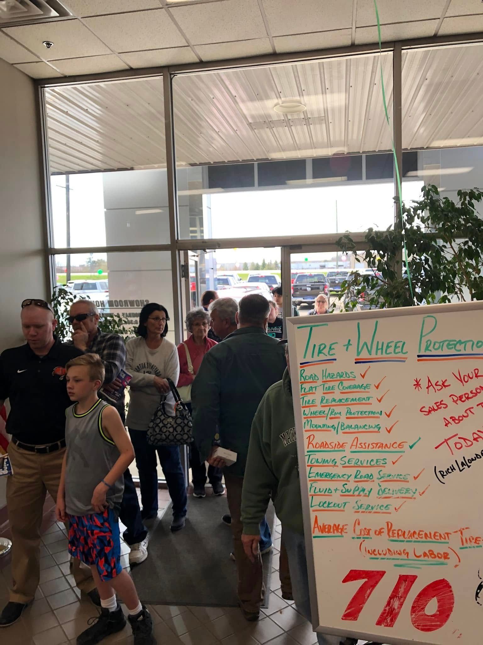 People standing inside a storefront near a white signboard with colorful handwritten sale notices.