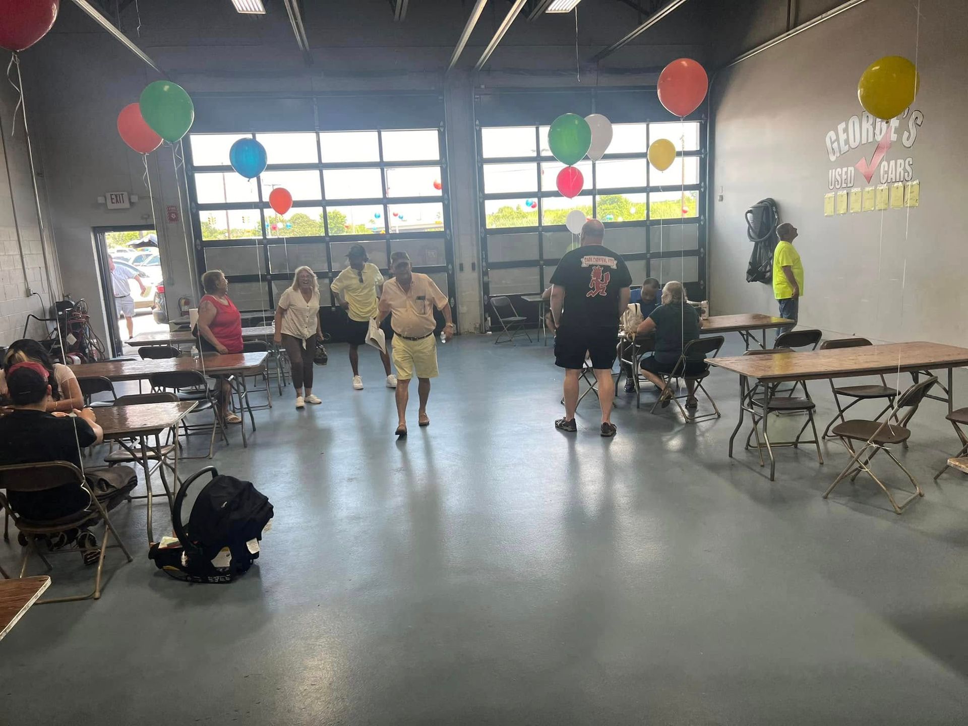 Indoor gym with people, tables, and colorful balloons near a bright entrance