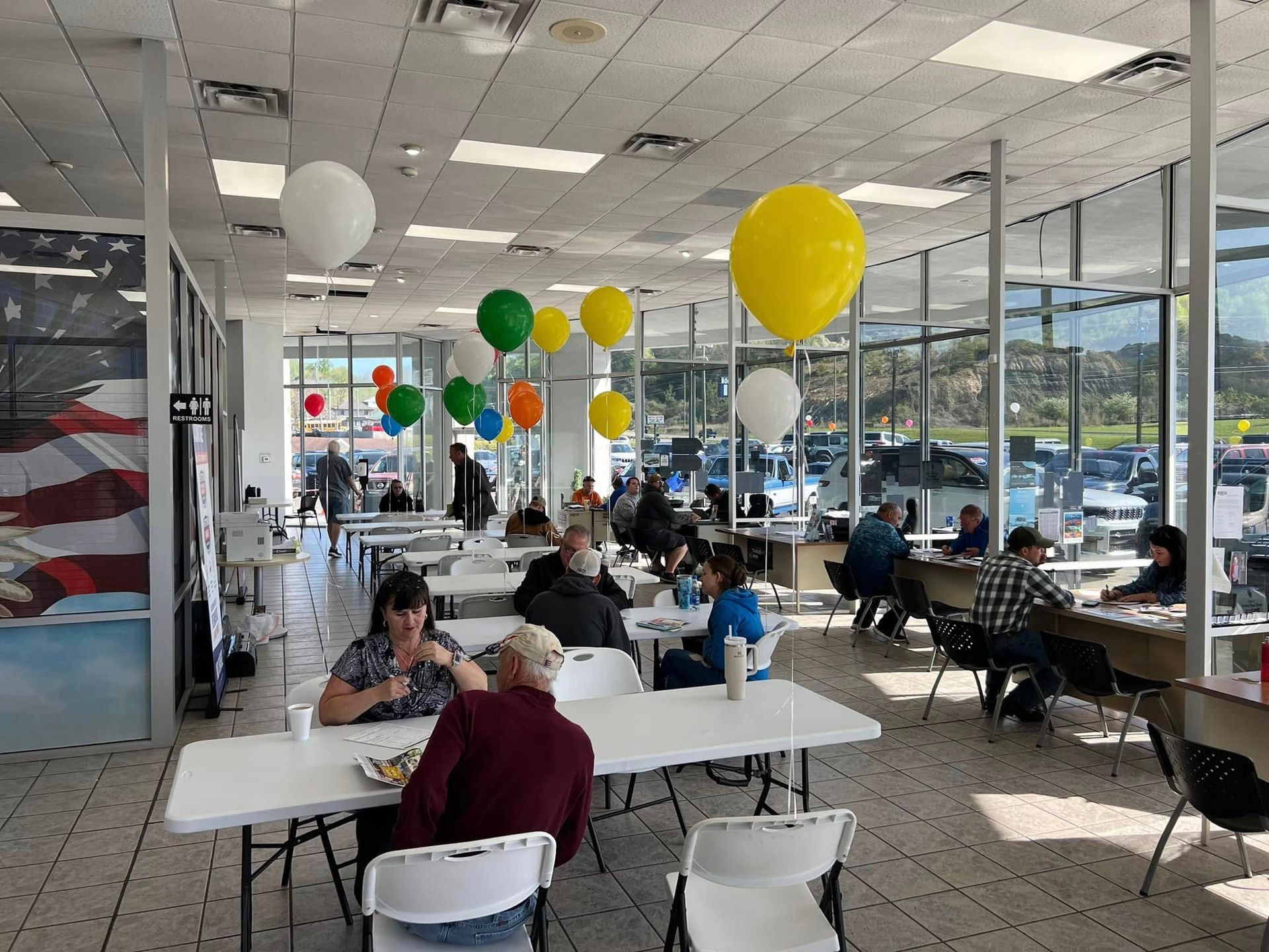 Bright office cafe with people seated at tables and colorful balloons hanging from the ceiling