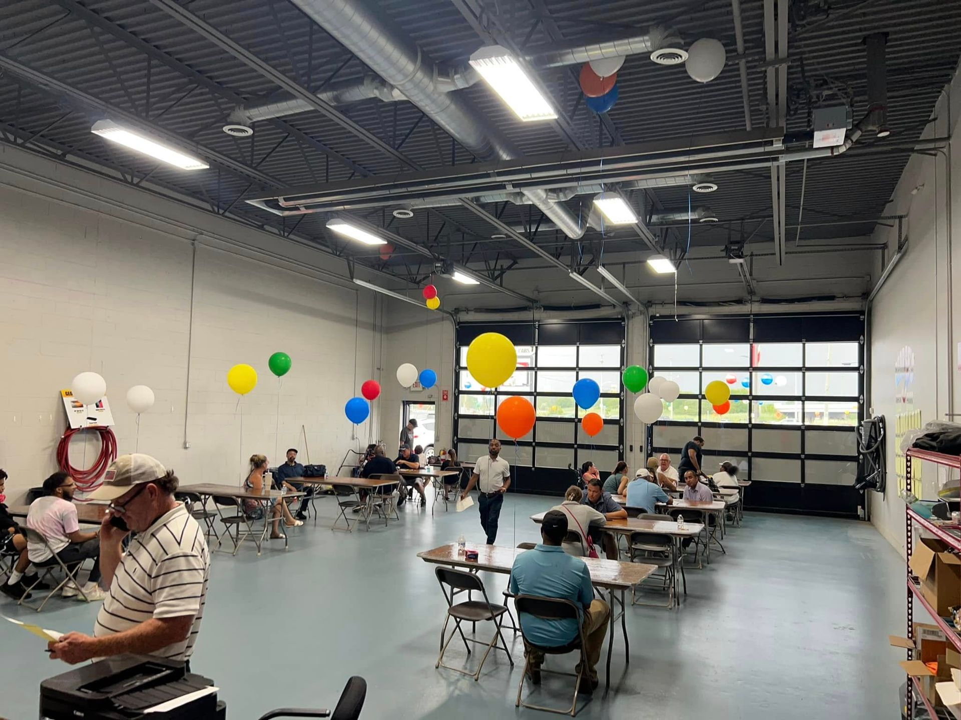 People seated at tables in a bright hall decorated with colorful balloons and streamers
