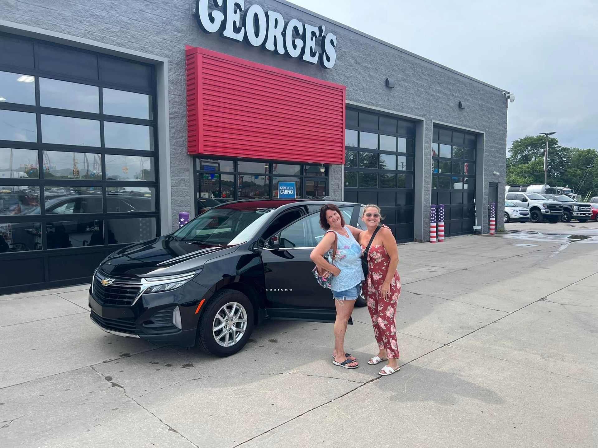 Two women standing beside a black SUV outside a George's storefront