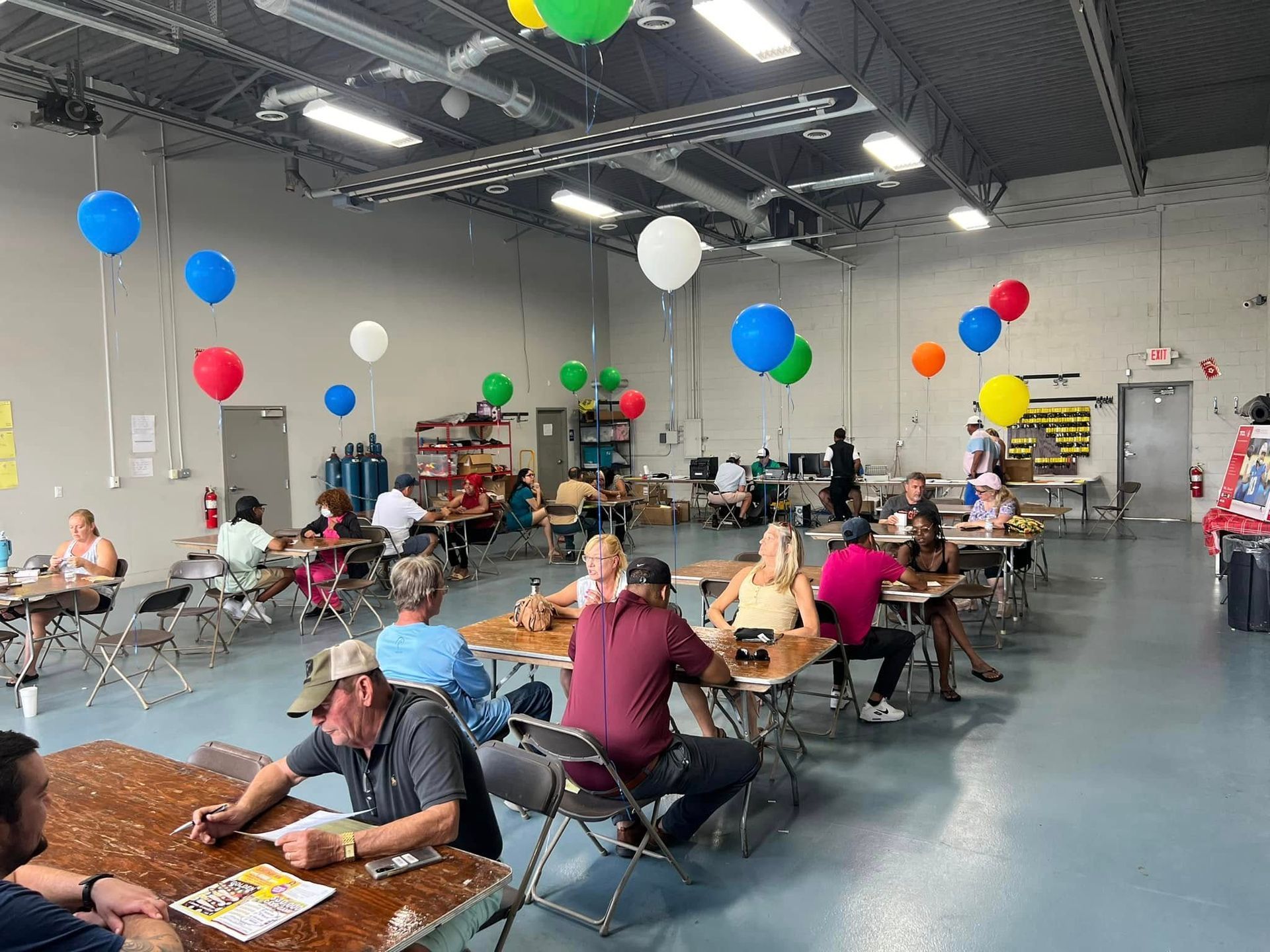 People seated at tables in a decorated indoor event hall with colorful balloons overhead