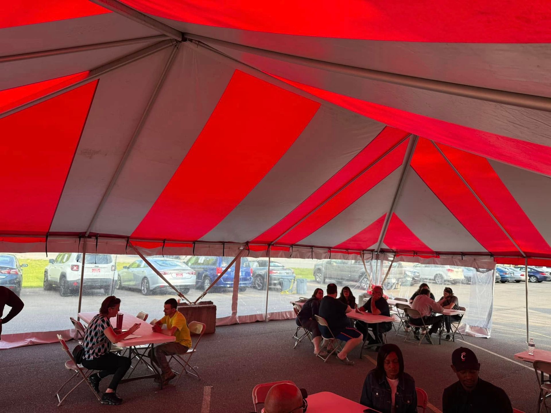 People seated at tables under a large red-and-white striped tent at an outdoor gathering
