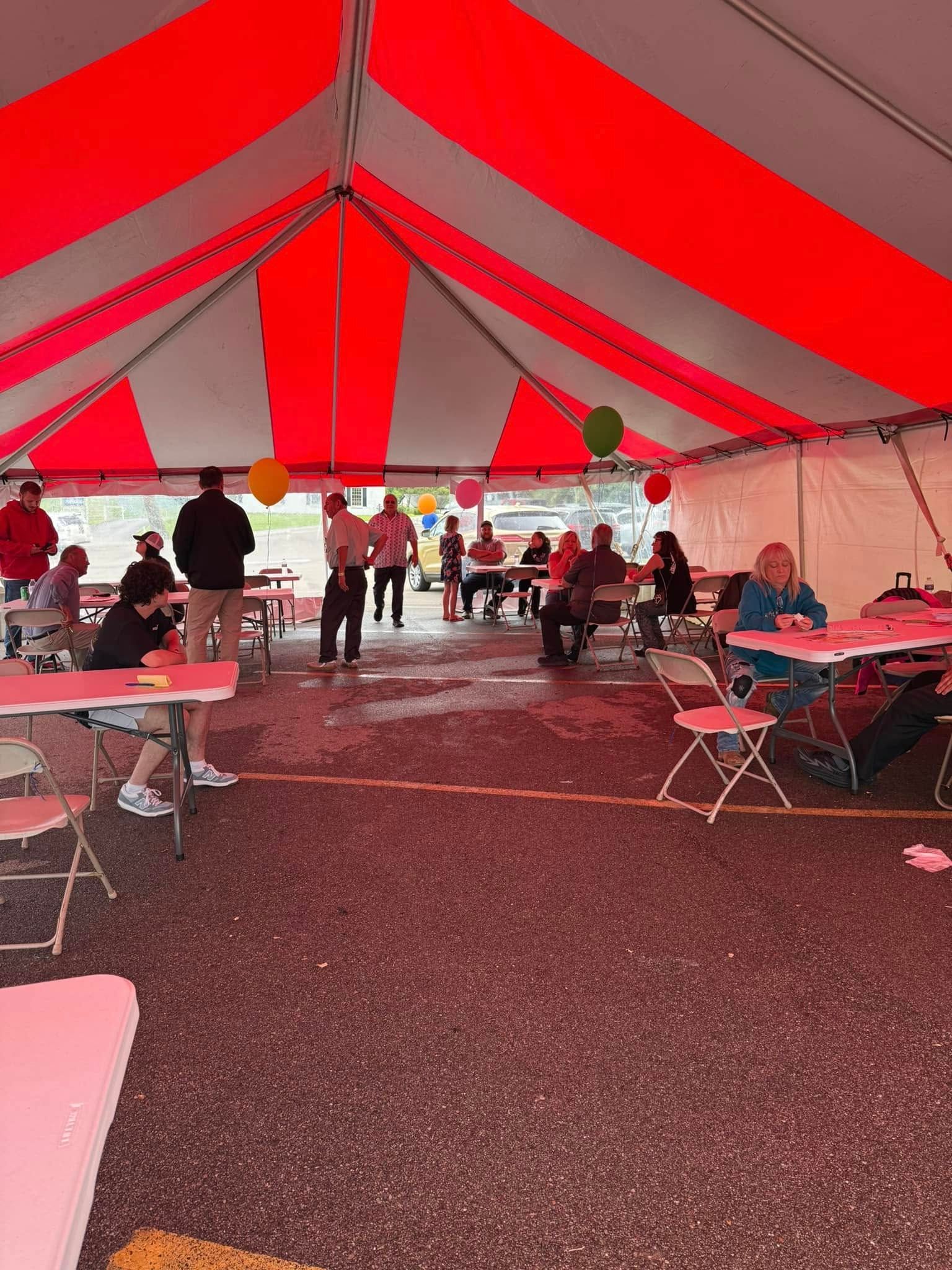 Large red-and-white tent interior with people standing and seated at tables on a gravel floor