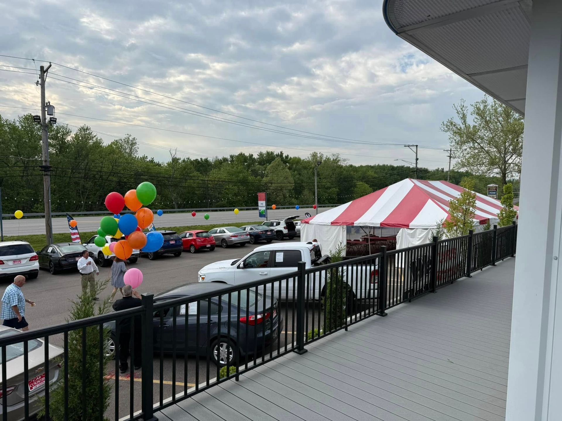 Outdoor parking lot with red-and-white tent, colorful balloons, and parked cars beside a balcony railing