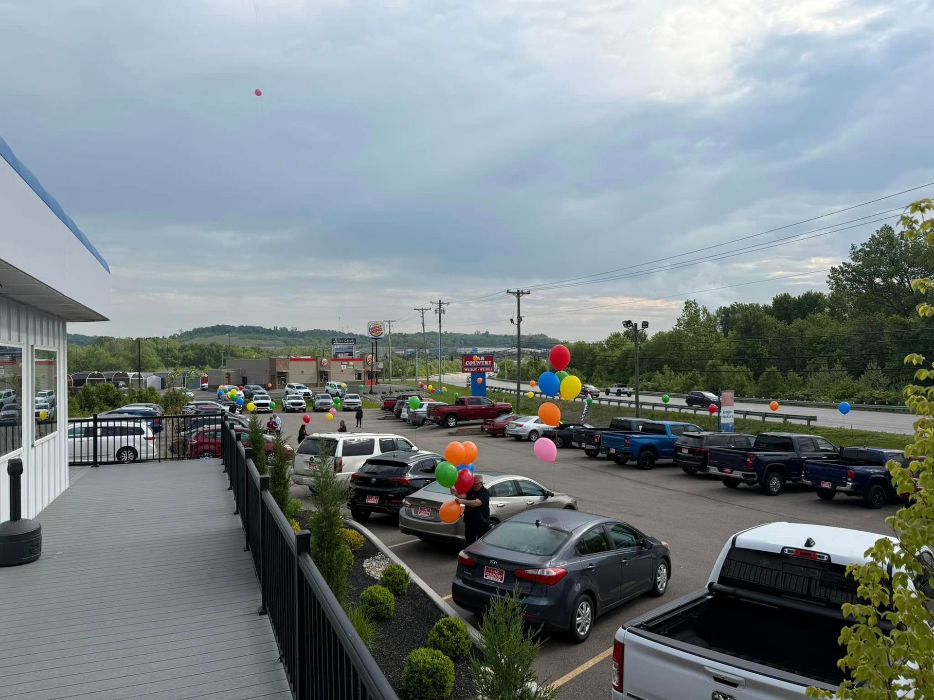 Parking lot outside a store with many cars, colorful balloons, and a cloudy sky