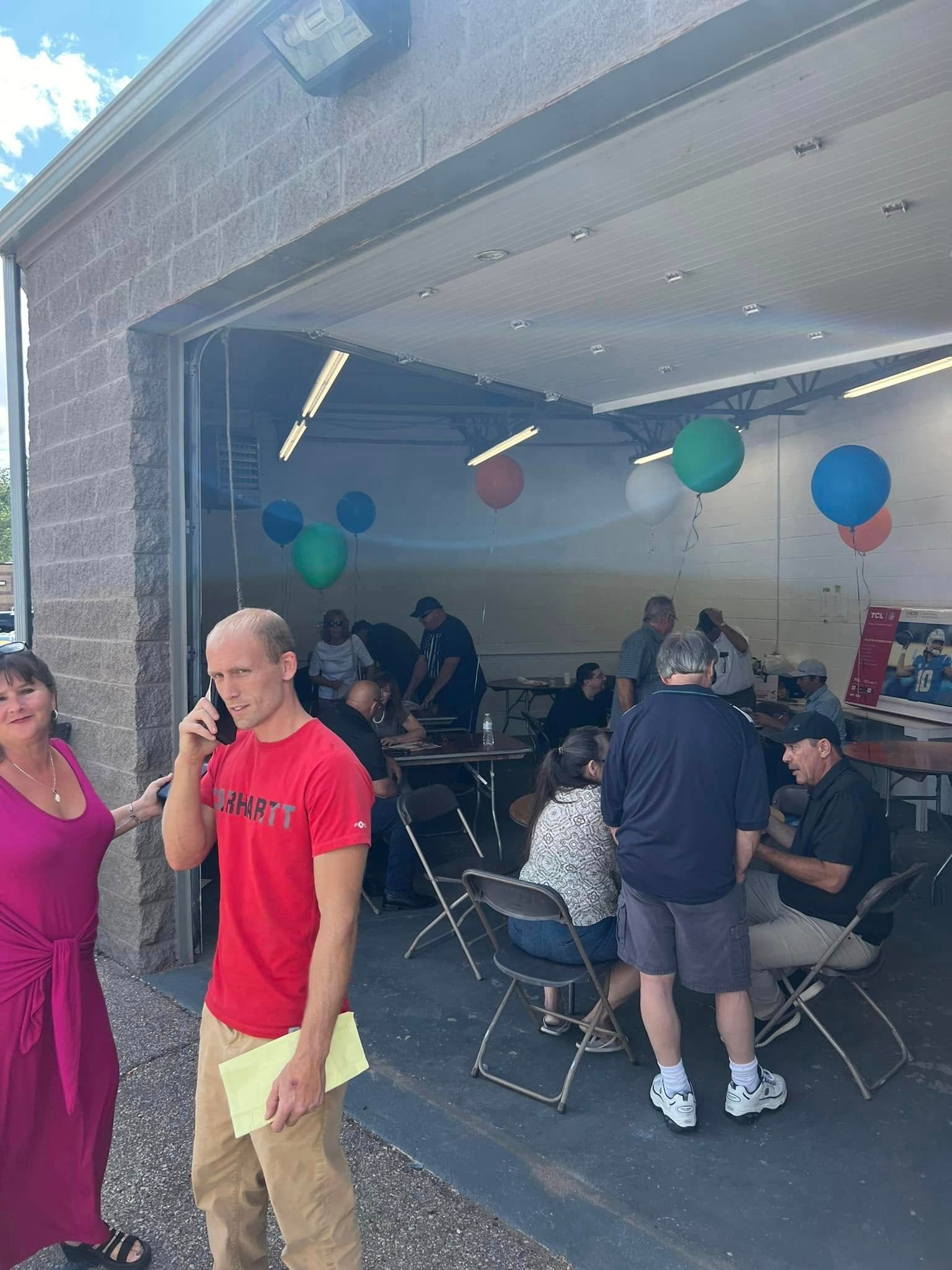 People gathered in a garage for a social event with blue and green balloons and folding chairs.
