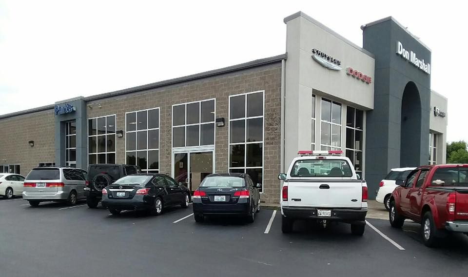 Car dealership lot with several parked cars in front of a modern service building