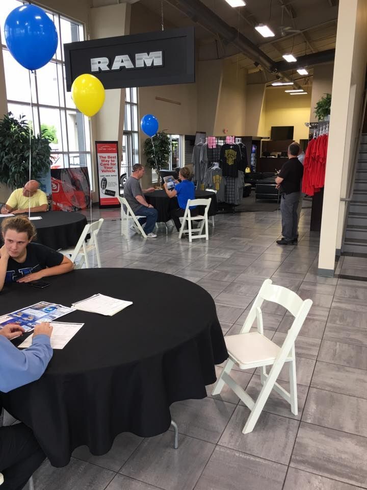 Indoor event booth with black tablecloths, white chairs, and blue and yellow balloons in a warehouse-like space