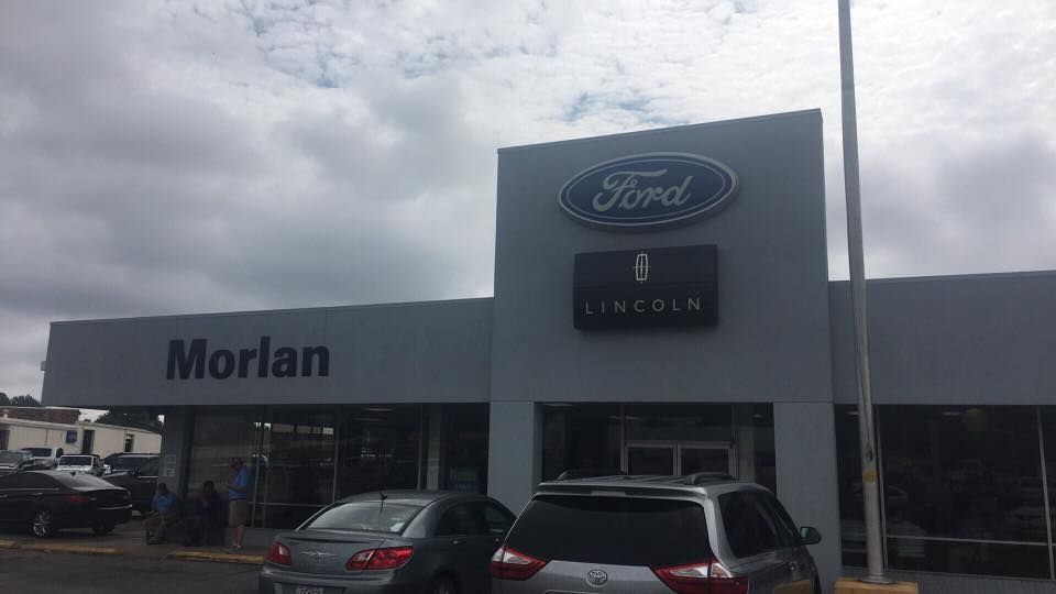 Ford dealership storefront with Morlan sign, parked cars, and cloudy sky