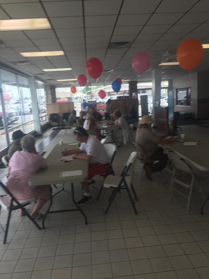 People seated at tables in a decorated indoor café or community space with colorful balloons hanging overhead.