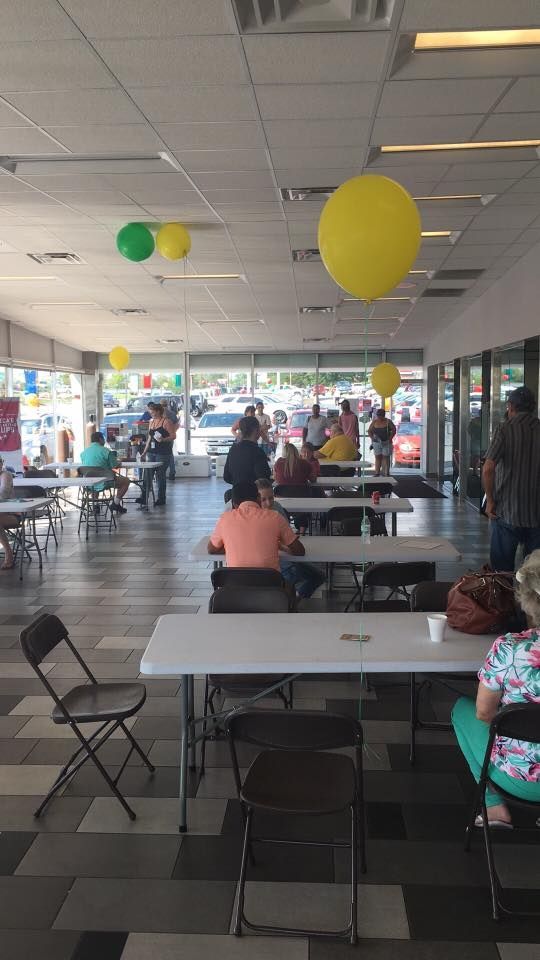 Indoor food court with people seated at tables under hanging yellow and green balloons.