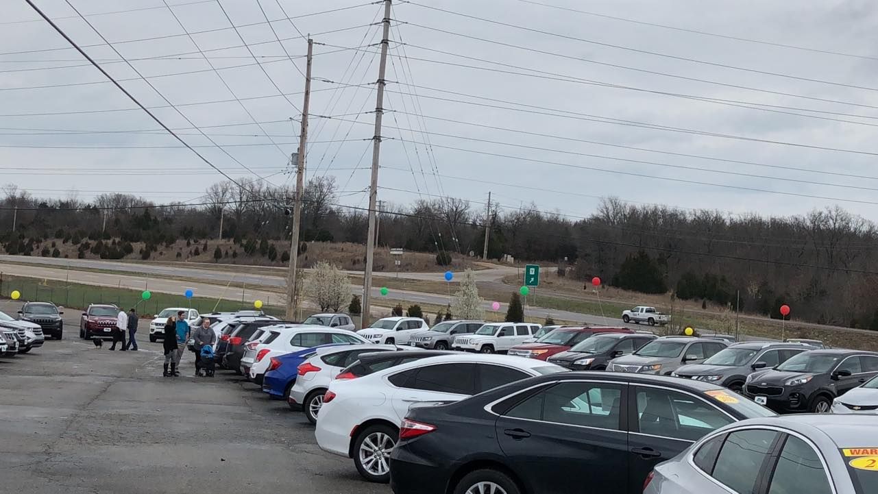 Crowded parking lot with rows of cars and a few people under a cloudy sky