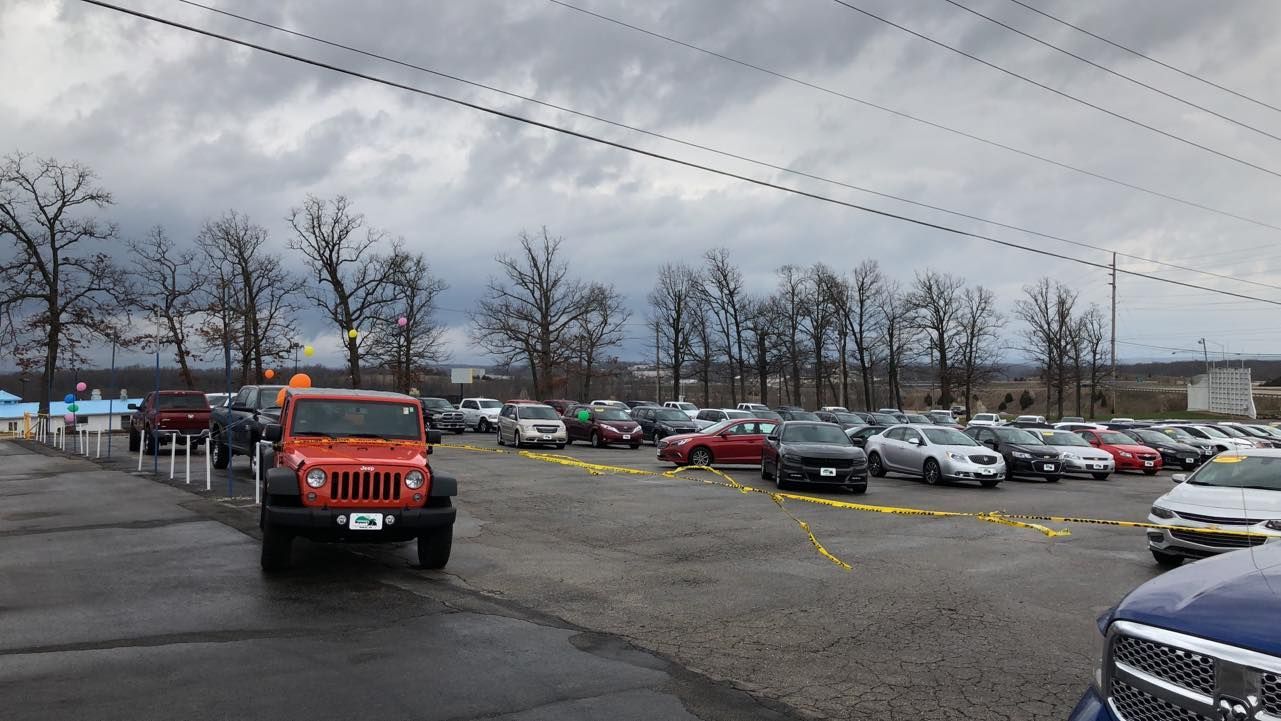 Orange Jeep in a wet parking lot with rows of parked cars under a cloudy sky