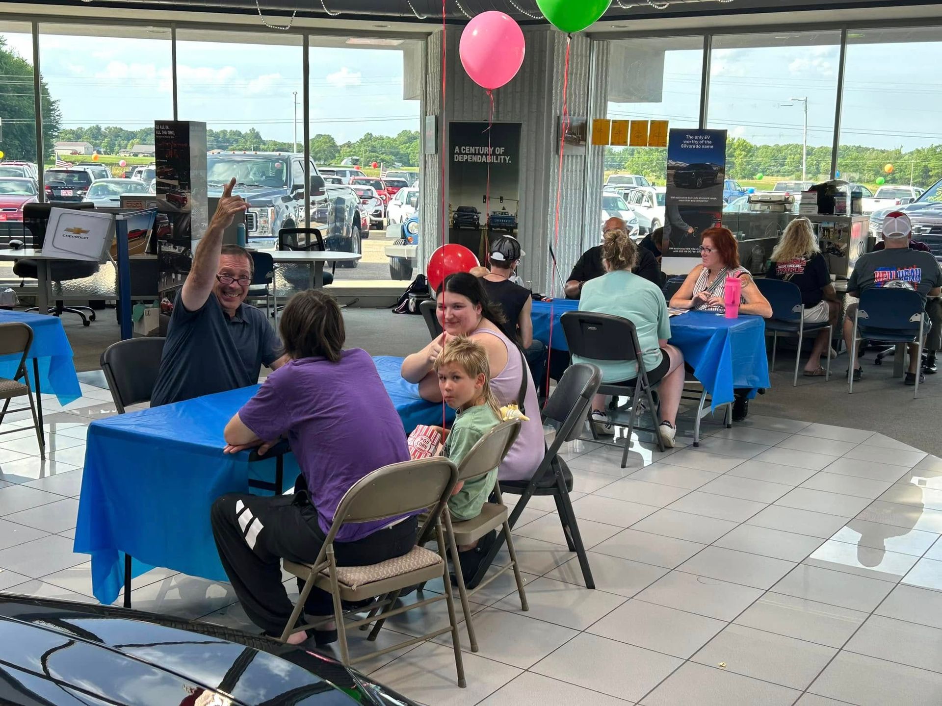 People seated at tables inside a bright restaurant, with balloons and a parking lot visible outside.