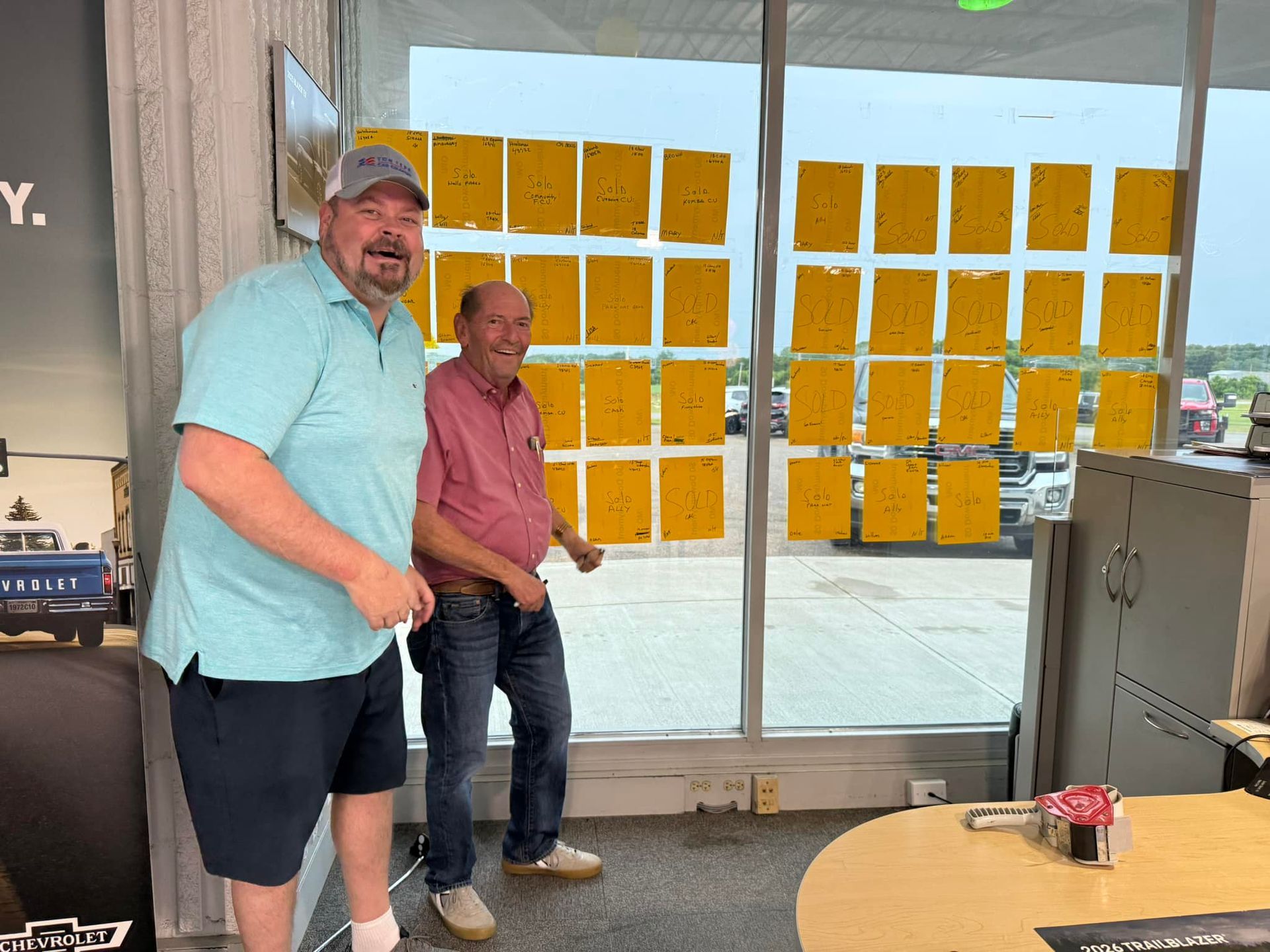 Two people stand in a glass-walled room with yellow sticky notes on the windows.