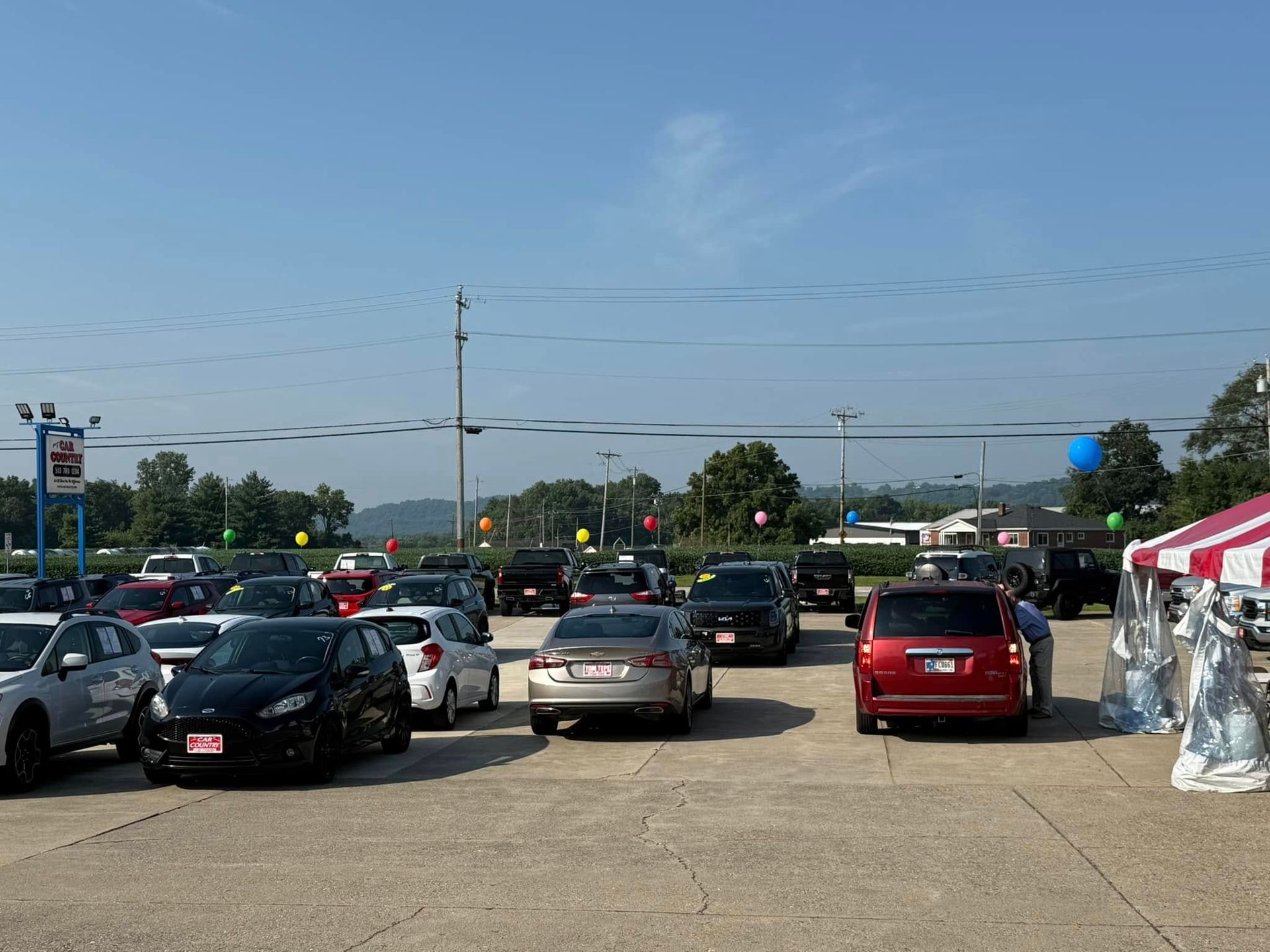 Parking lot full of cars under a clear blue sky, with a red-and-white tent on the right.